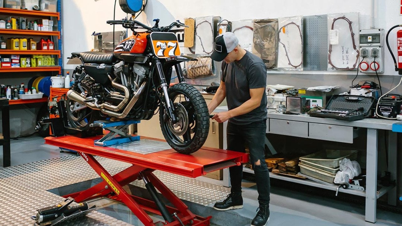 Unrecognizable mechanic man checking engine of custom motorcycle over platform.