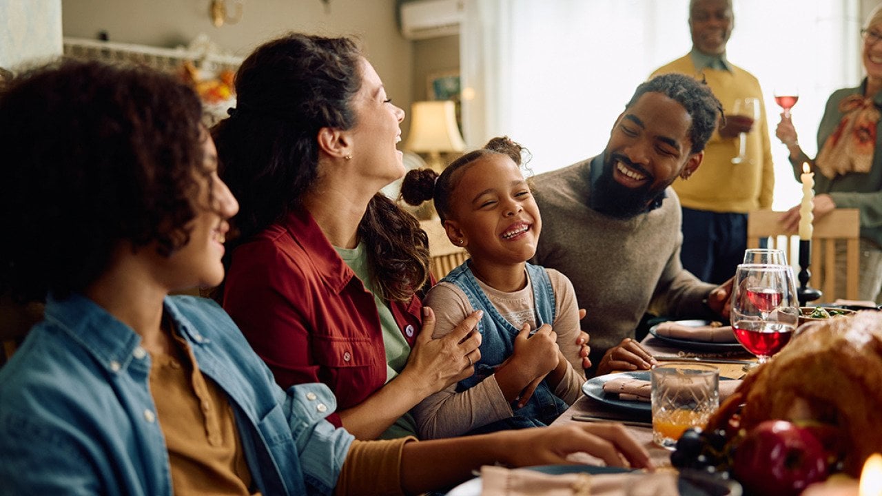 A big family laughing during Thanksgiving dinner at home.
