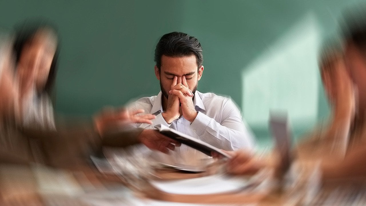 A male employee seated at the center of an office table with his surroundings are illustrated with a motion blur.