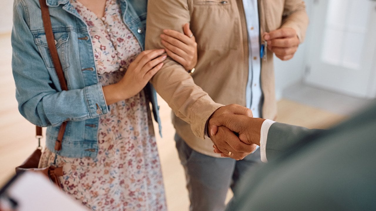 A couple shaking hands with a real estate agent after purchase.