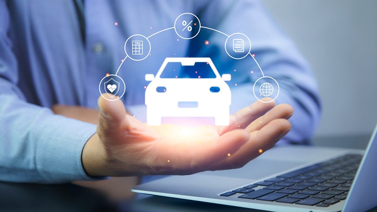 A car insurance agent using a laptop with graphics of car insurance concepts illustrated over his hand.