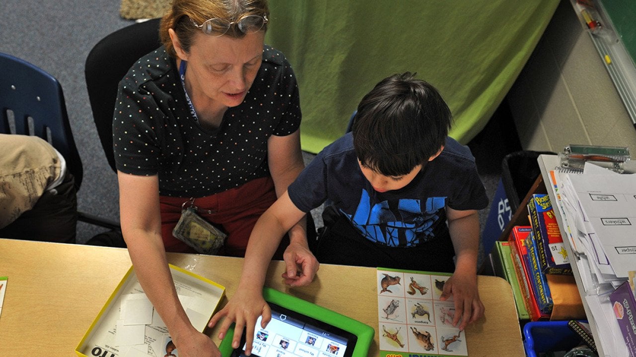 An instructional assistant helping an autistic student with a lesson or activity from a tablet.