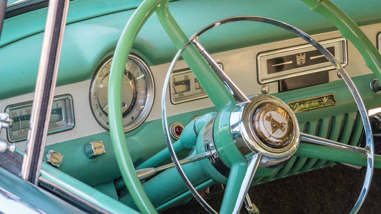 A close up view on a vintage pastel green car's steering wheel.