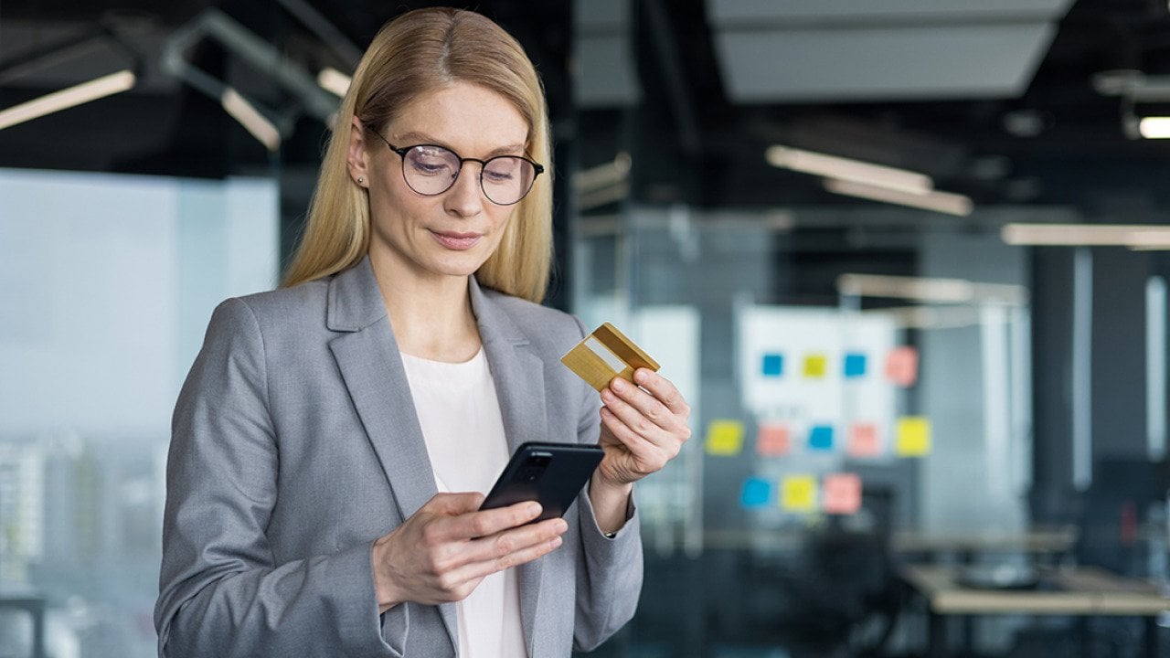A businesswoman holding a phone and a credit card in an office.