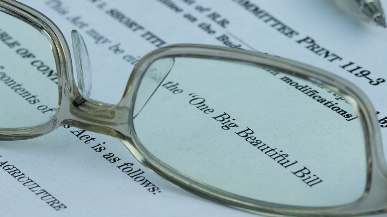 A pair of eyeglasses magnified on the words 'One Big Beautiful Bill' (Act) on a document.