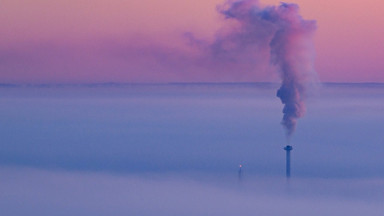 Smoke coming out of a heat and power plant chimney, blending with a lavender morning sky.