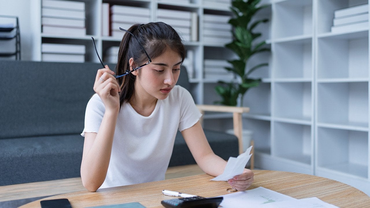 A confused young woman reviewing financial documents at her home office.