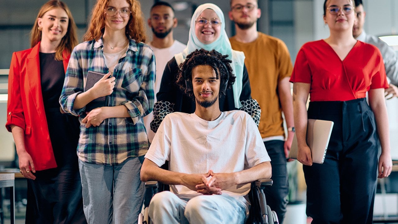 A diverse group of young business people, with a person in wheelchair at the center, showcasing community and accessibility.