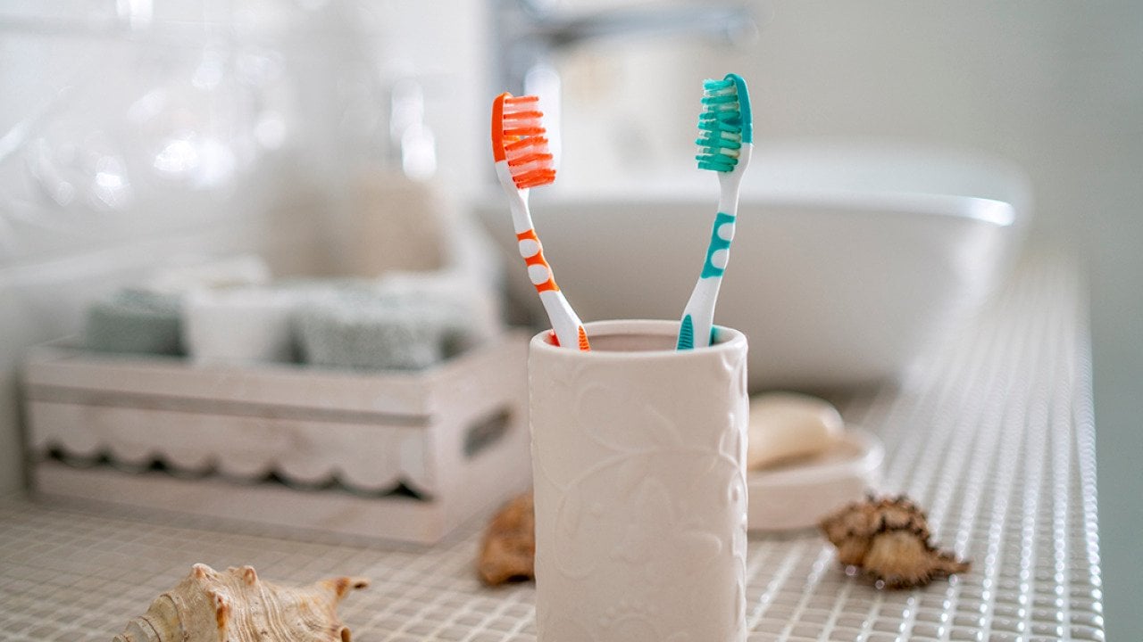 Two colorful toothbrushes in a ceramic glass against the background of a bathroom's washbasin.