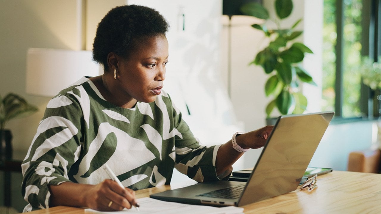 A black female bookkeeper working with a laptop and financial reports at home.