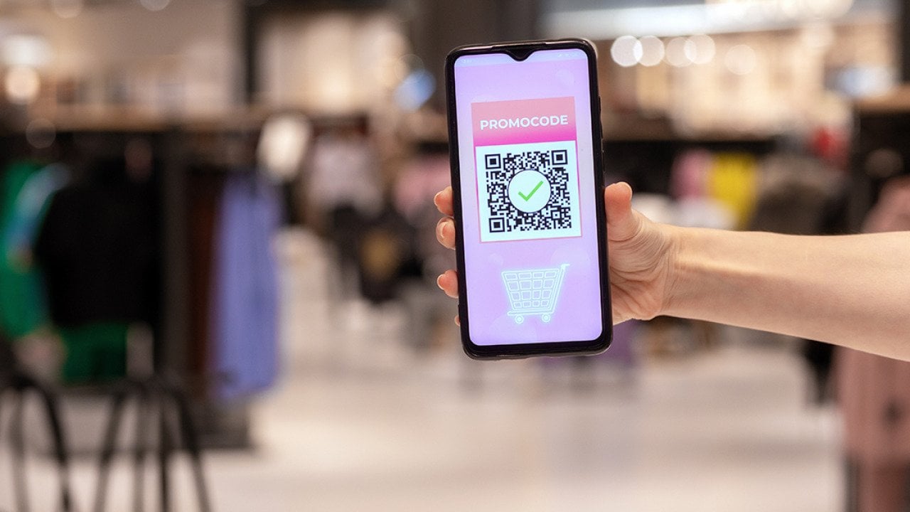 A woman's hand holding a phone displaying promo code applied by scanning a QR code inside a shopping mall.
