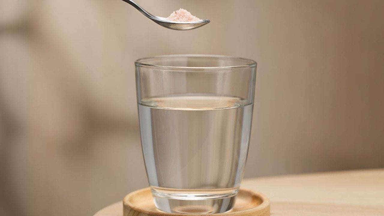 A spoon of Himalayan salt held above a glass of drinking water, highlighting its potential health benefits.