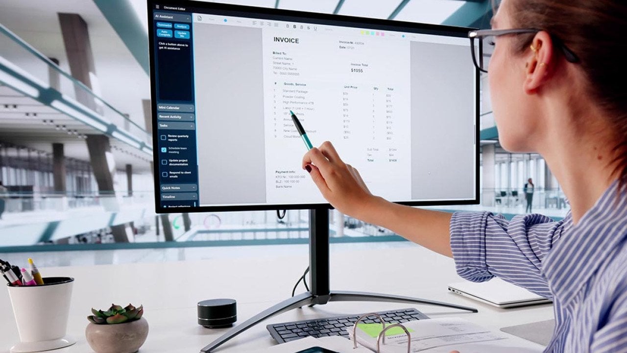 Person pointing out line item on invoice on large computer monitor.