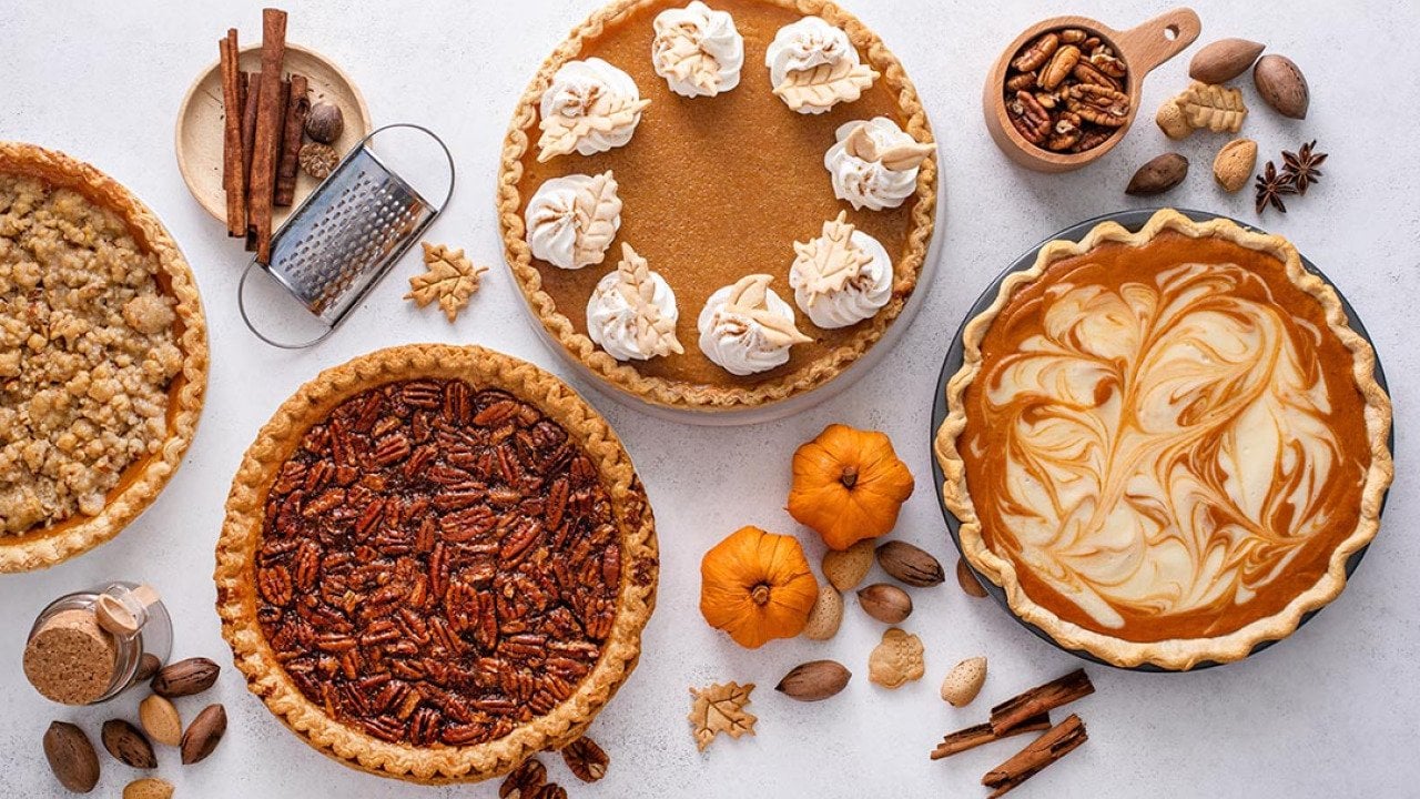 Top-down view of variety of Thanksgiving pies including pumpkin, pecan and cheesecake pumpkin pie on light background.