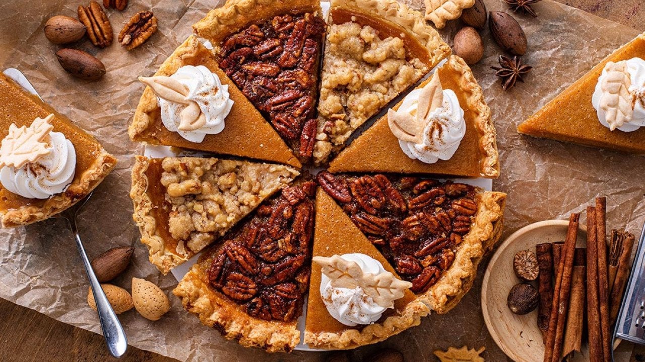 A pie composed of alternating slices of pumpkin with whipped cream and pecan pie, on parchment paper. 