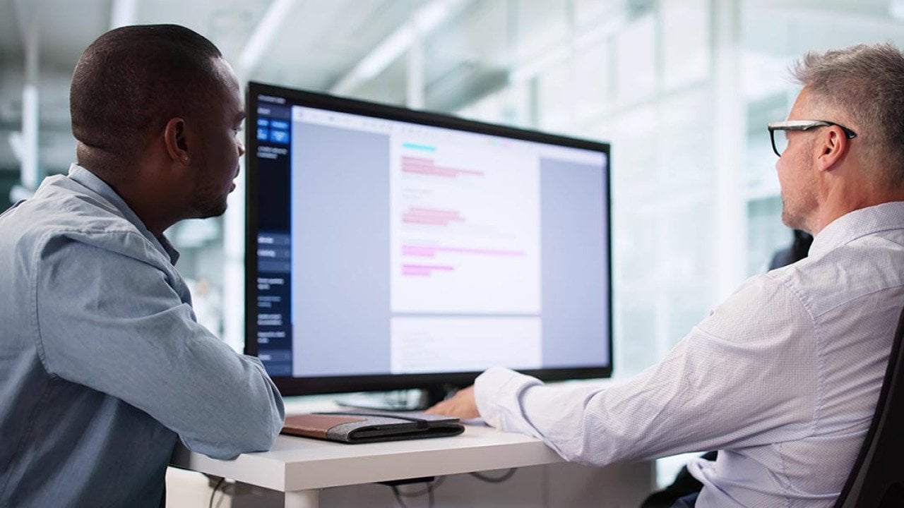 Two people sitting at a desk looking at a large screen; one is a privacy compliance specialist ensuring HIPAA regulations are being followed correctly.