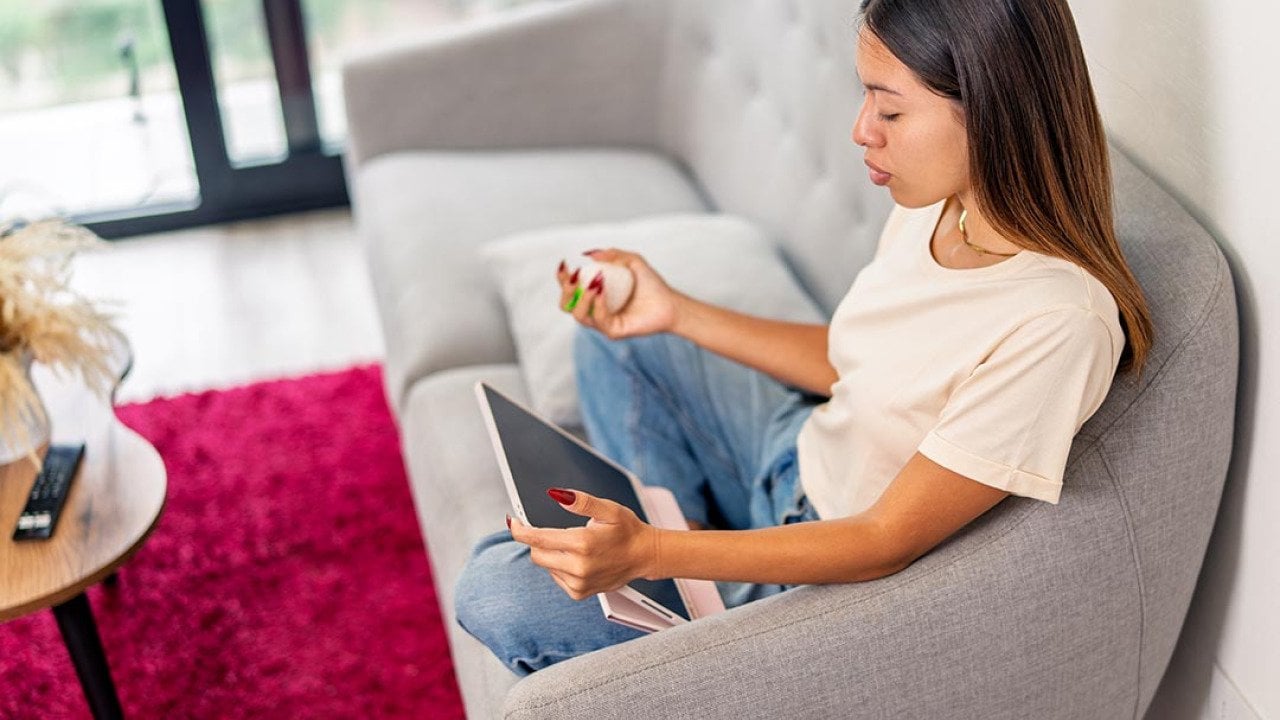 A neurodivergent young woman sitting comfortably on sofa, using digital tablet managing mental health in home environment.