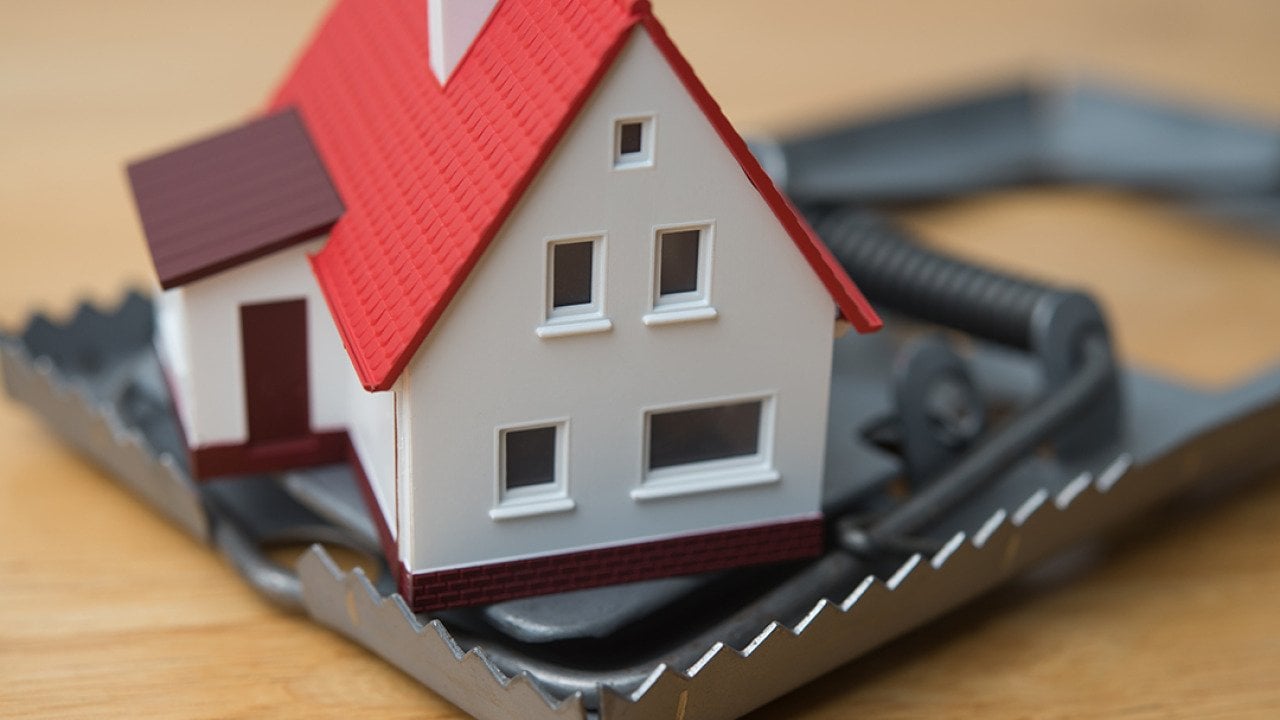 Mortgage scam concept depicted by a figure of a house inside a steel trap.