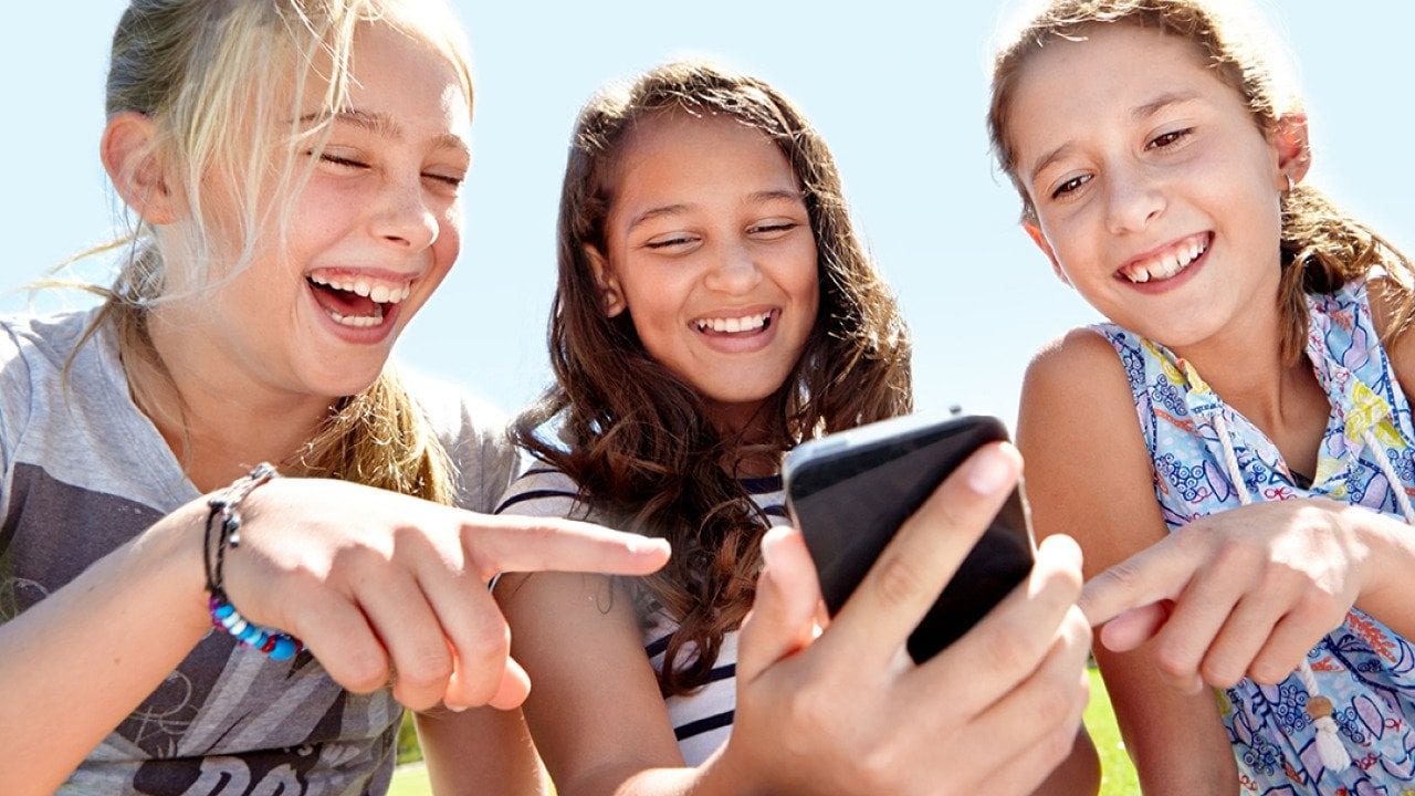 A group of three young girls laughing at content on social media.
