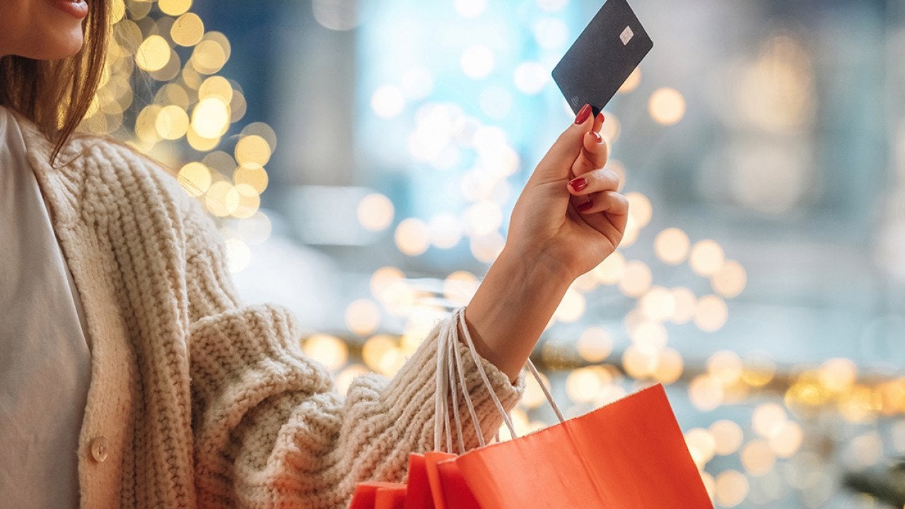 A woman with shopping bags on her arm and holding up a credit card.
