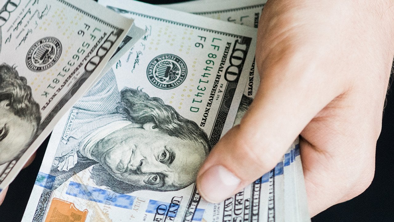 A person's hand counting $100 dollar bills.