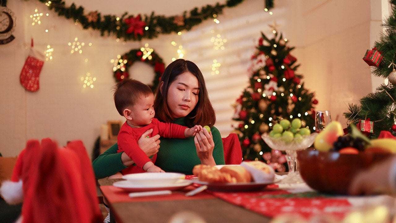 A young mother sitting alone with holding her baby at the dinner table during Christmas Eve.