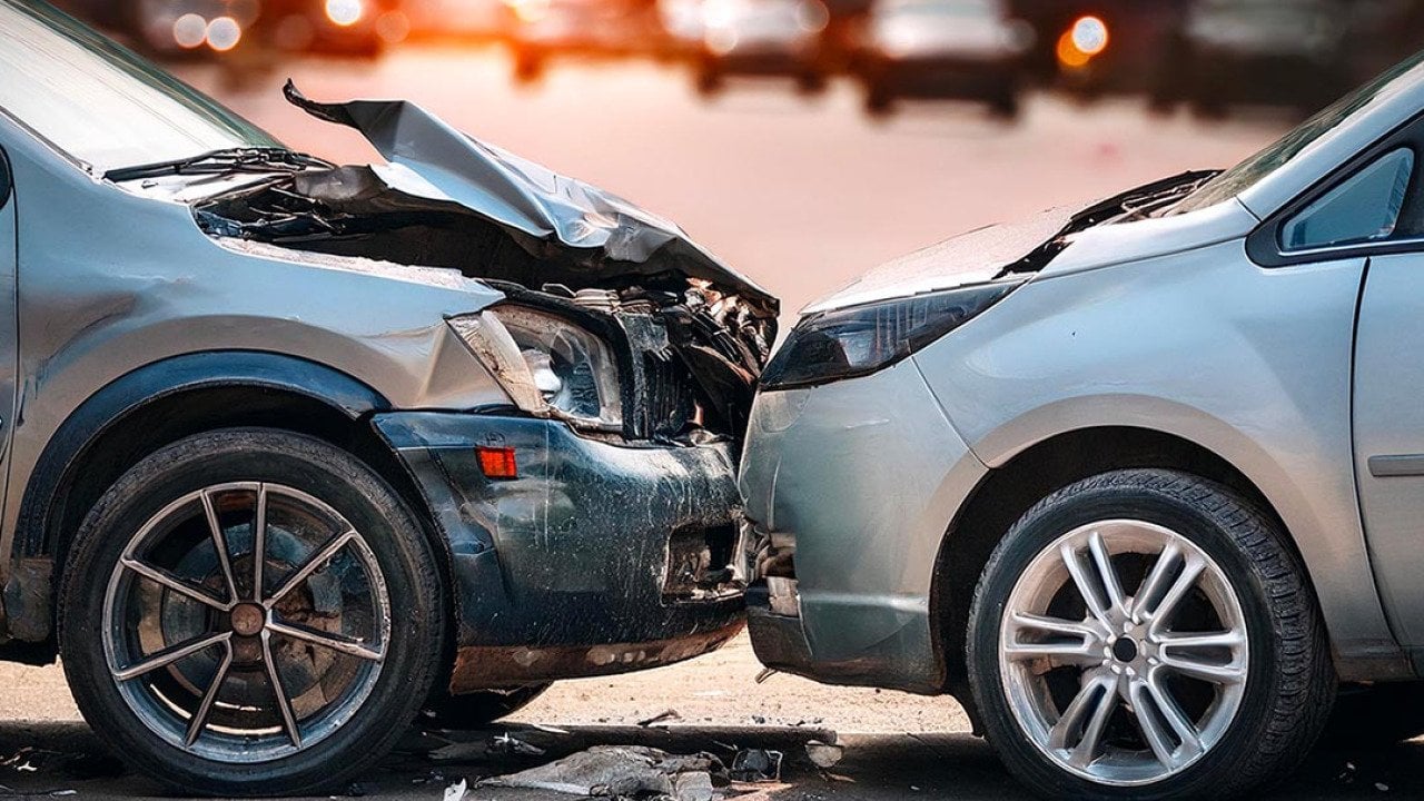 Side view of two silver cars that are stopped in a collision with the hood of one car visibly damaged.