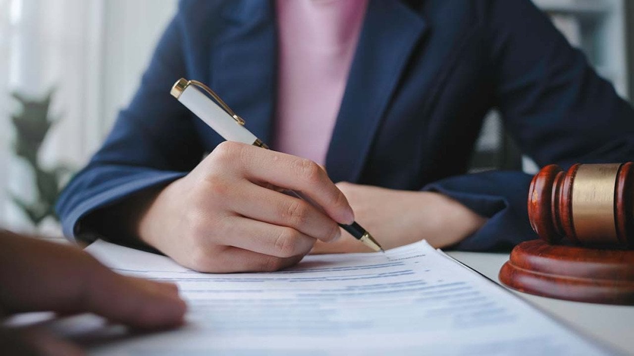 Torso of a female lawyer signing a document for a client in their office.