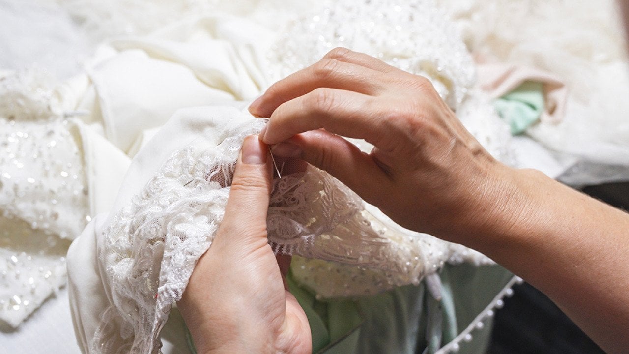Hands of a seamstress sewing beads on a wedding dress.