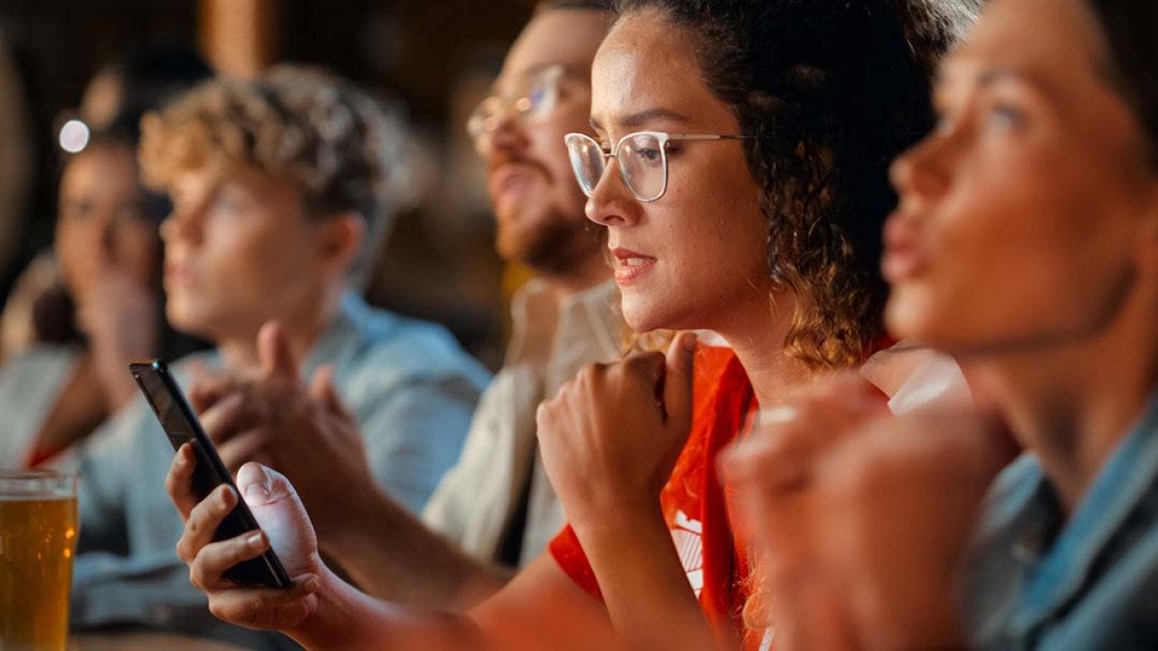A female football fan in a bar monitoring game results on her phone.