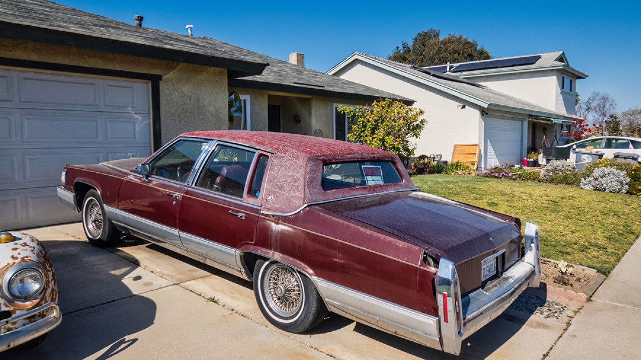An old red vintage car parked on the driveway of a home.