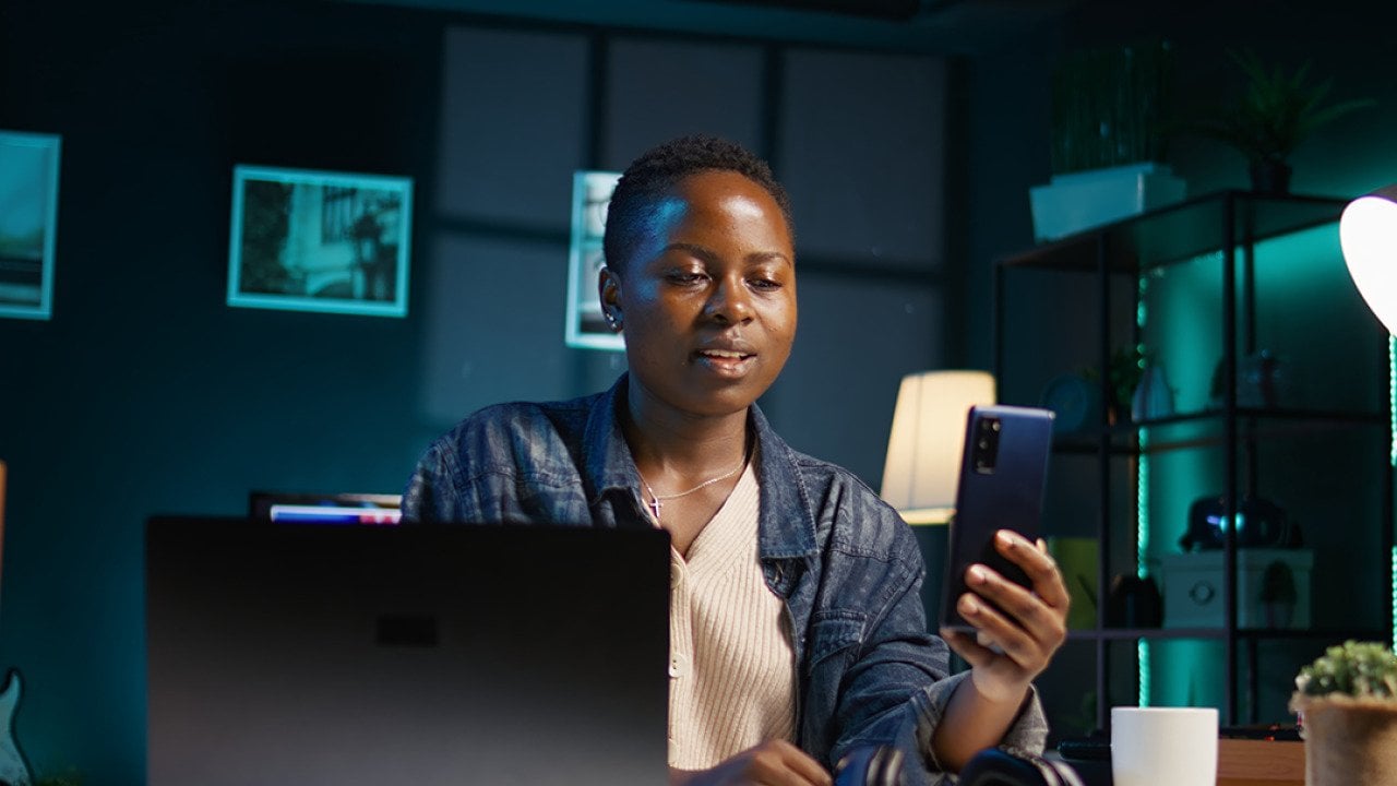 A black female professional answering a video call on her phone while working from home.