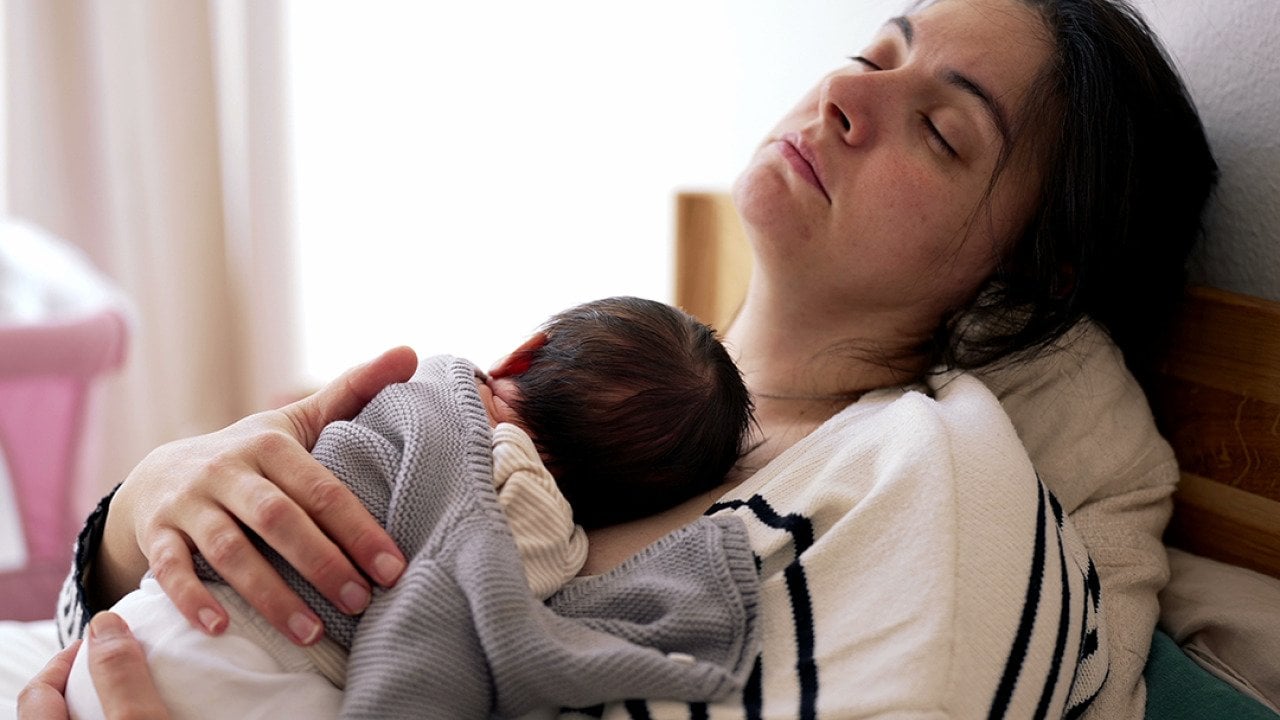 A tired mother sleeping with her newborn on her chest.