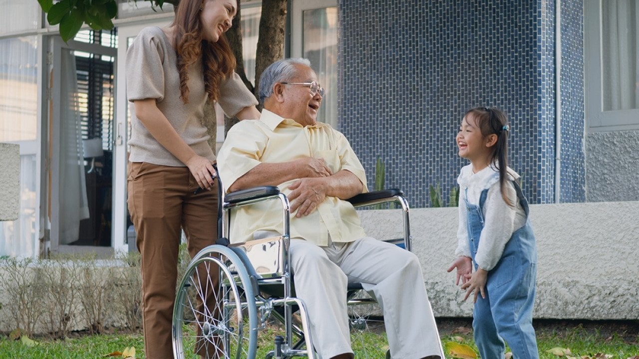 A disabled senior grandfather with his daughter and grandchild in a park.