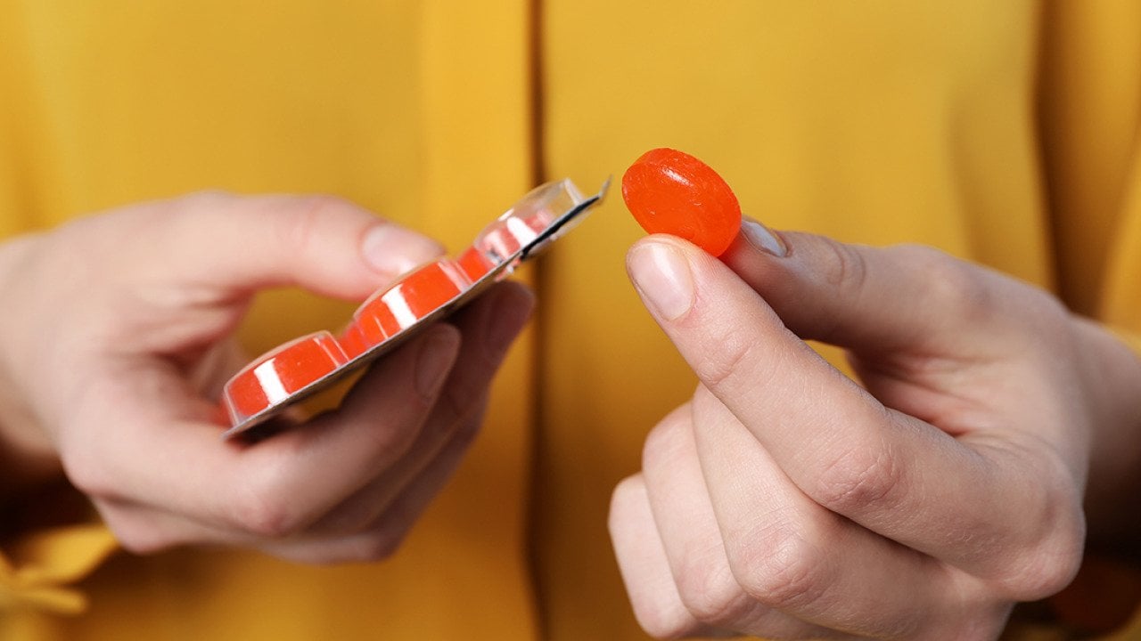 A woman holding a red cough drop tablet.