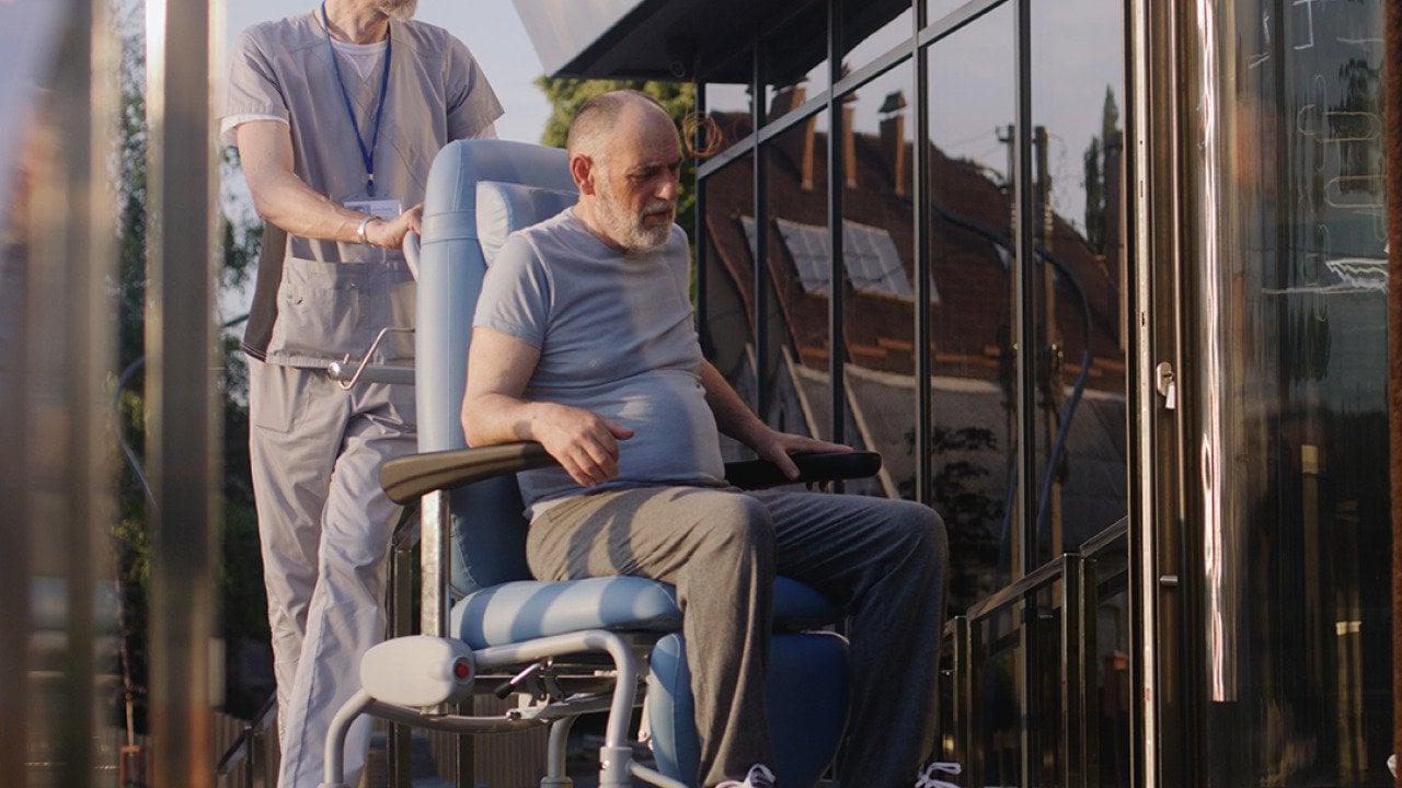 Two doctors assisting a disabled elderly man to the clinic entrance.