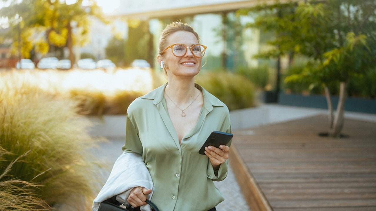 A businesswoman heading to work with a briefcase and listening to wireless earphones.