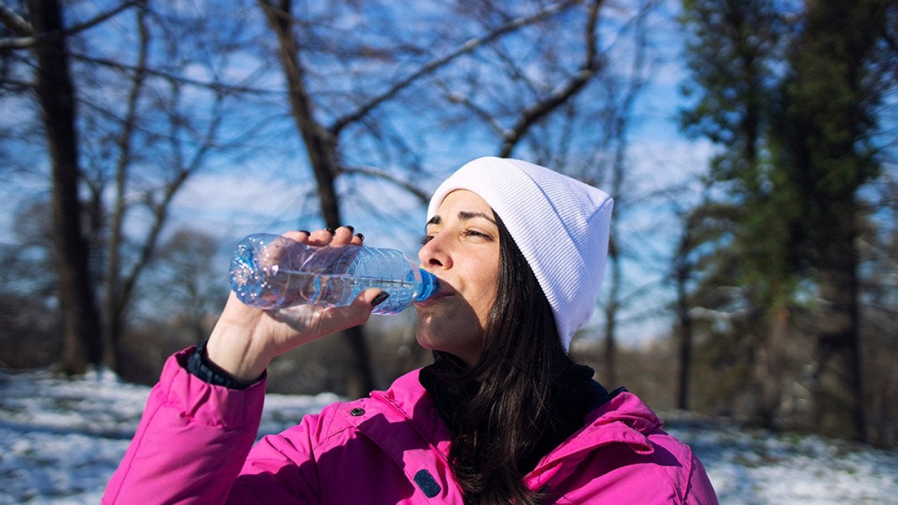 A female athlete in winter clothes drinking water outdoors.