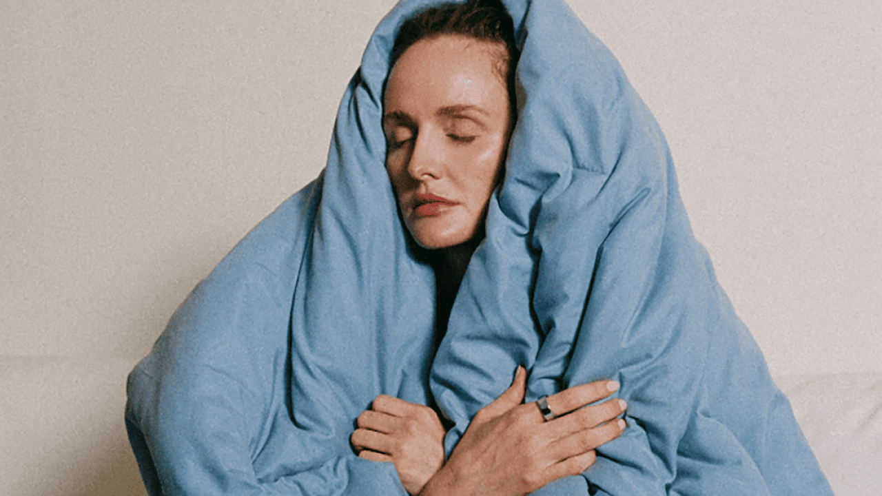 A sleepy woman covering her head with a blue blanket.