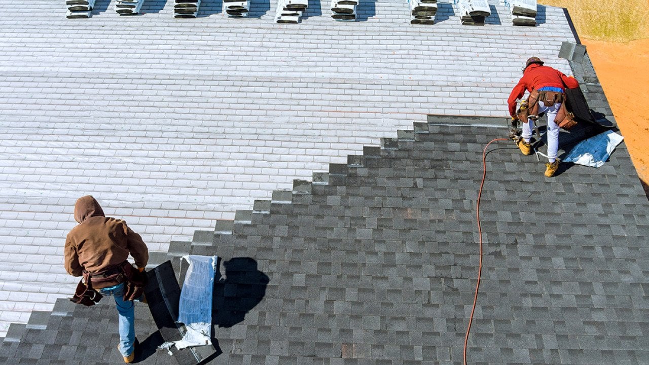Aerial view of roof workers installing shingles using hammer and nail.