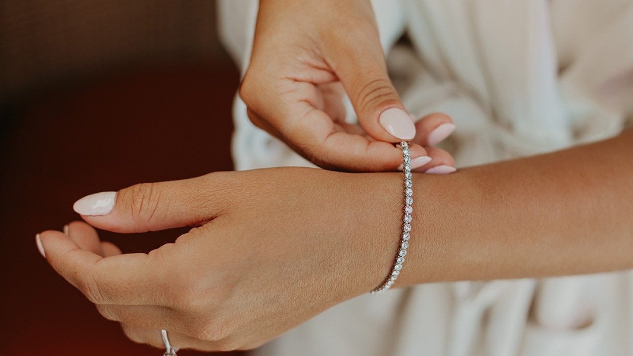 A bride putting on an elegant bracelet on her left wrist.