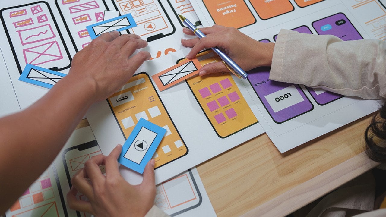 Web designers arranging cutouts to visualize a mobile app interface project.