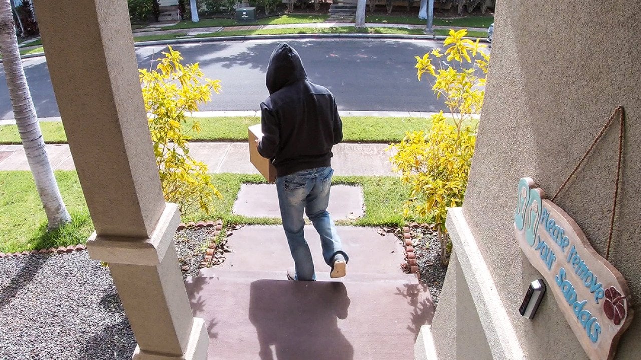 A surveillance camera-view of a package thief walking away from a porch after taking a package.