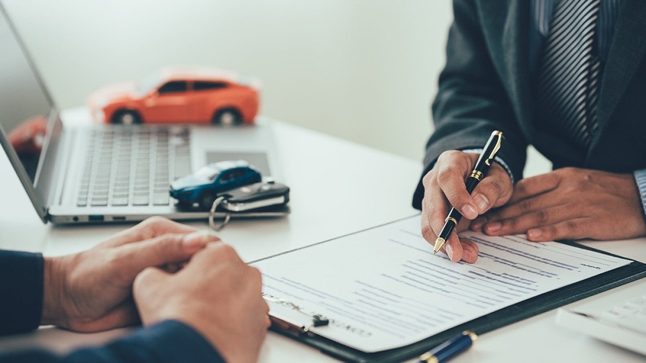 Figures of cars surround a table while a car salesperson transacts with a customer.