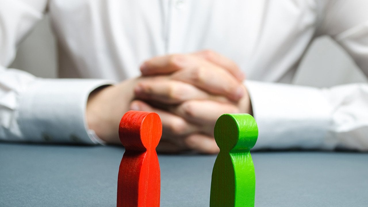 An arbitrator visualizing conflict situation between people depicted by two wooden figures.