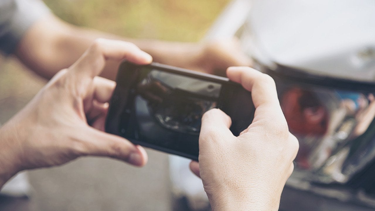 An insurance agent taking a photo of a car's damage.