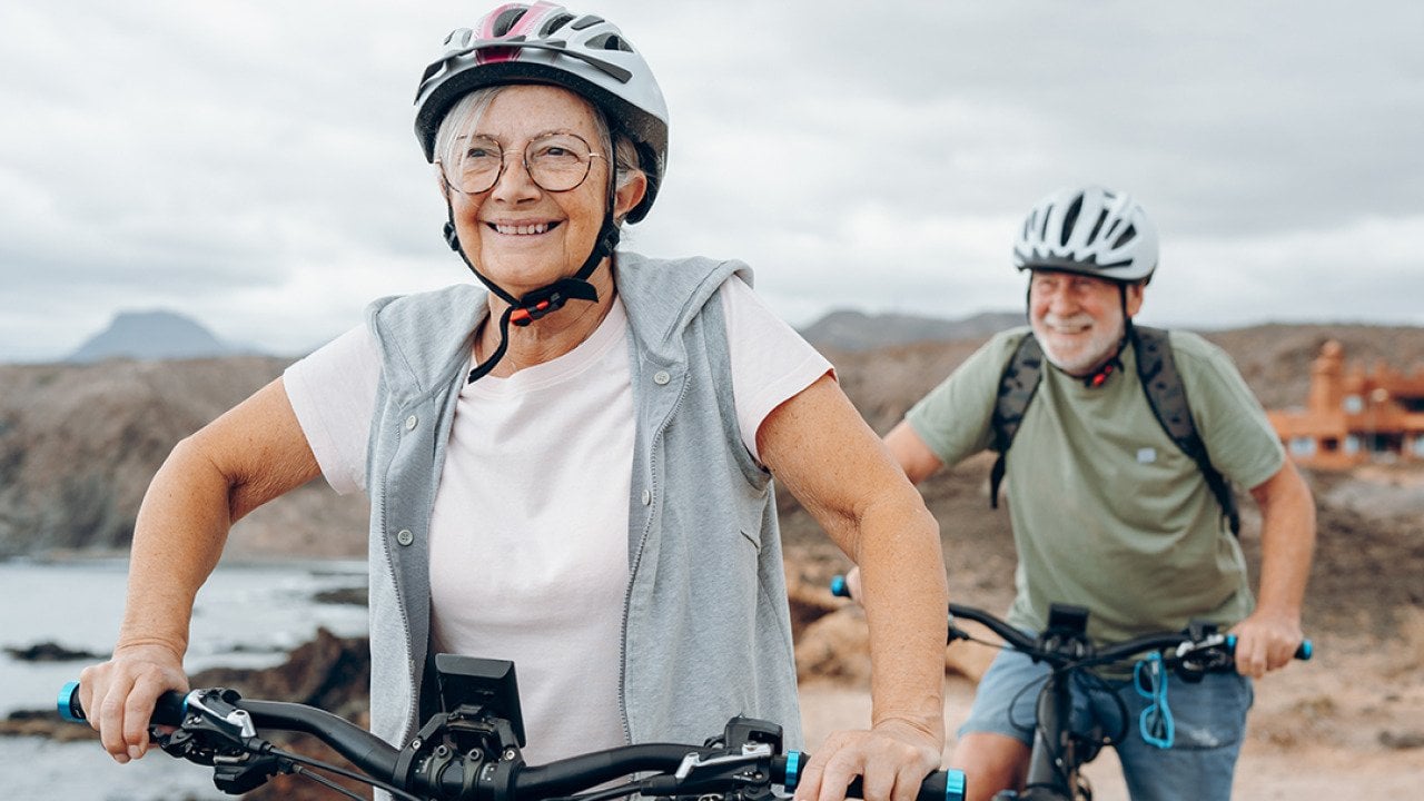 A senior couple riding their bikes on the beach.