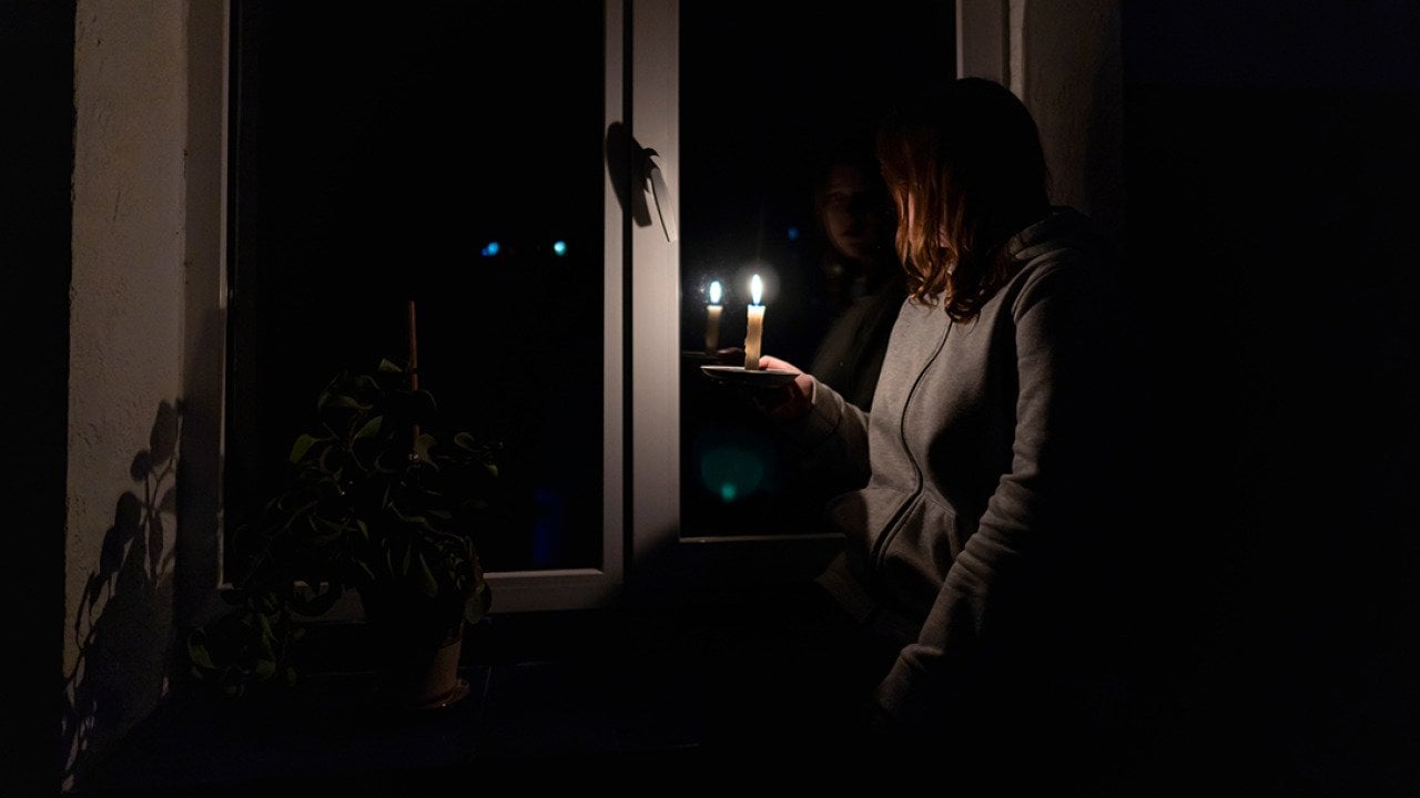 A woman standing by the window holding a candle during a power outage.