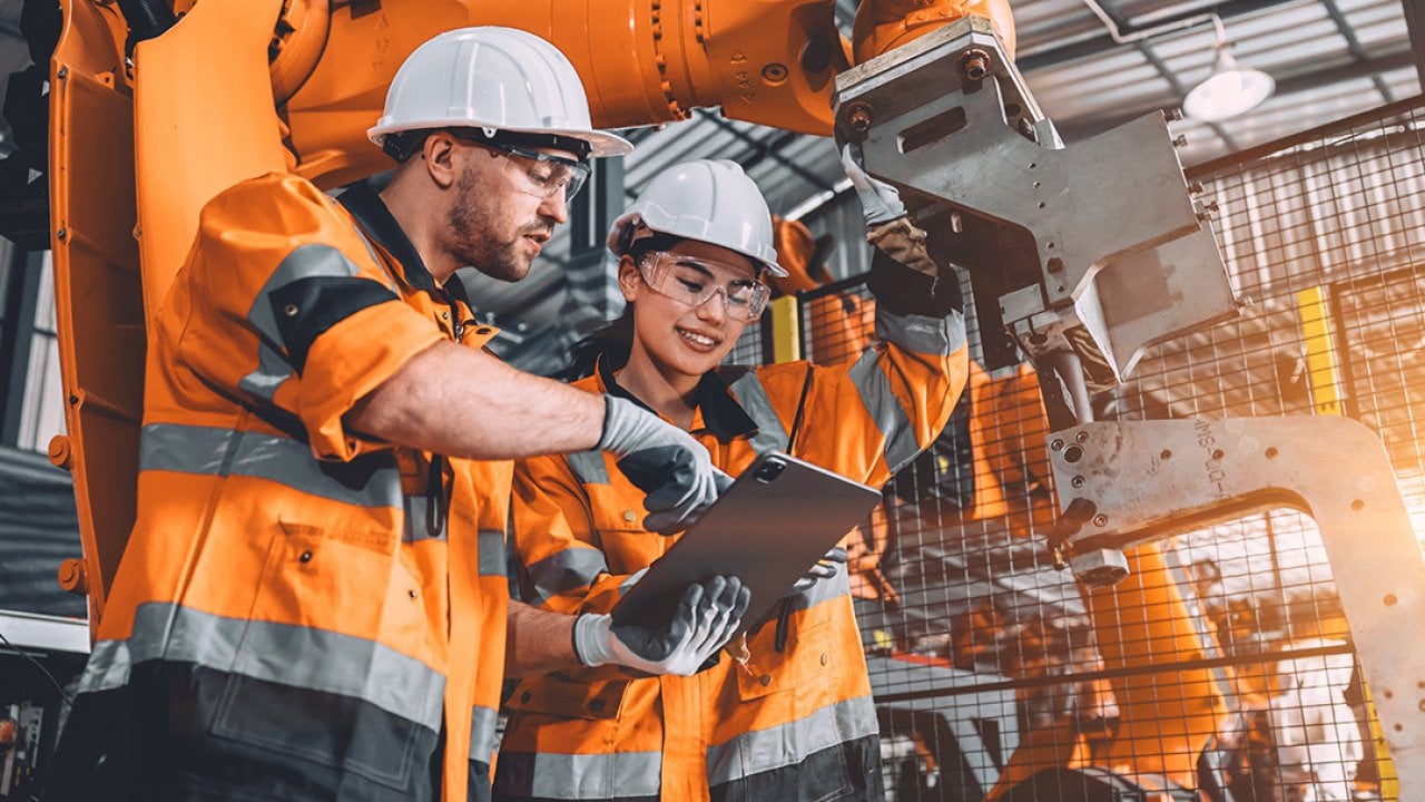 Two members of an engineering team looking at programming in a tablet inside their automated manufacturing factory.