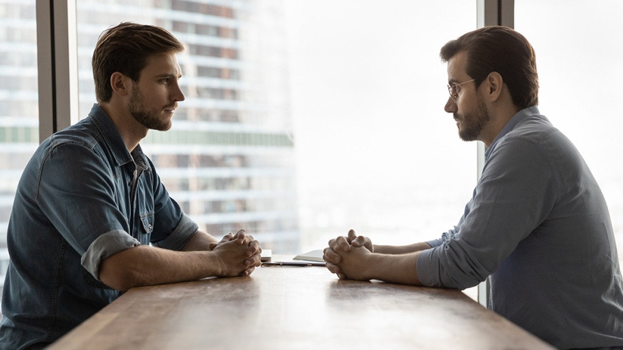 Two businessmen sitting across a table from each other engaged in discussion.
